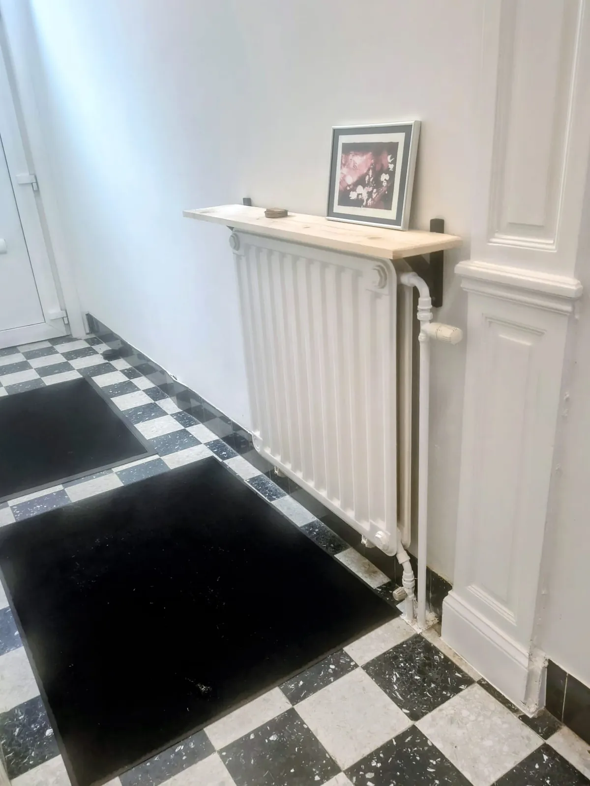 De gedeelde gang met de originele zwart-witte terrazzovloer en het witte paneelwerk